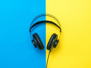 Black headphones with wire on yellow and blue background.