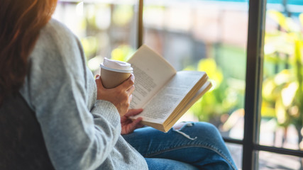 Closeup image of a woman reading book and drinking coffee in the morning