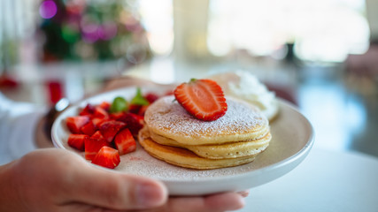 A woman holding and showing a plate of pancakes with strawberries and whipped cream