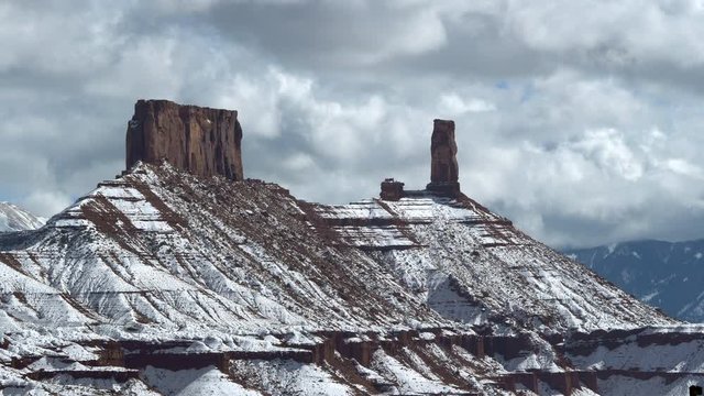View of snow covered Castleton Tower with dramatic clouds near Moab Utah in the desert during winter.