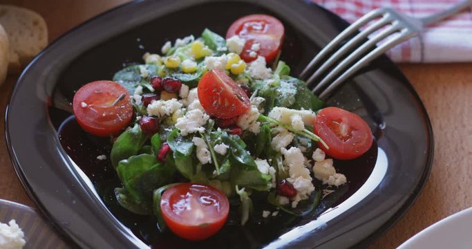 Fresh made corn salad with cherry tomatoes, soft cheese, sweetcorn kernel and pomegranate seed on plate on rotating stand, close up