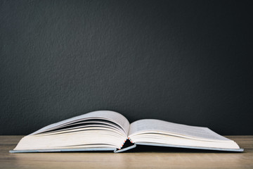 An old book open on wooden table with black color wall background and light frome above, copy space