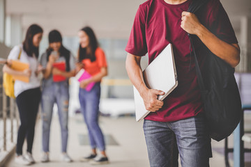 Obraz premium Education concept - Teens in the university and modern technology. Close up holding hand student a laptop and group of friends standing in the back.