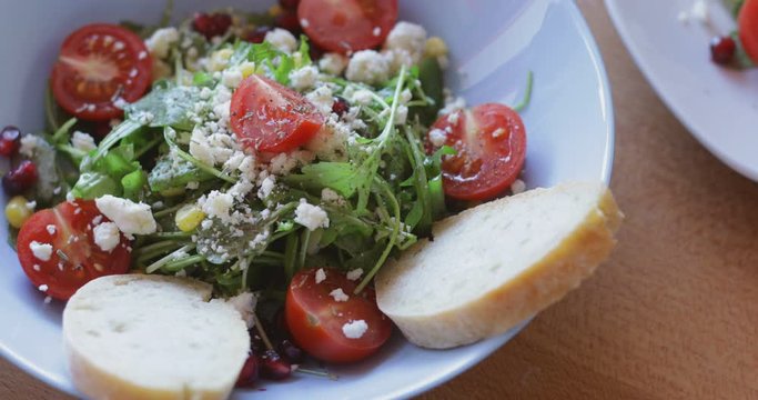 Fresh made arugula salad with cherry tomatoes, soft cheese, sweetcorn kernel and pomegranate seed on plate on rotating stand, close up