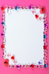 Valentine's day frame on pink background made of pebbles in the shape of a heart with white space and paper hearts.