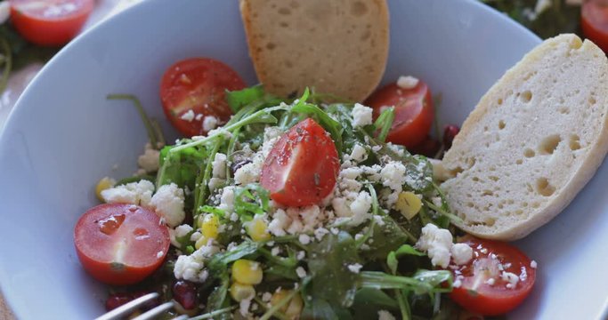 Fresh made arugula salad with cherry tomatoes, soft cheese, sweetcorn kernel and pomegranate seed on plate on rotating stand, close up