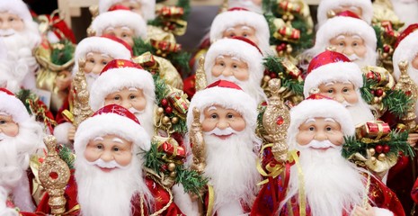 Army of Santa Clauses toy figures in red suits with presents and sticks. Merry Christmas background soft focus photo.