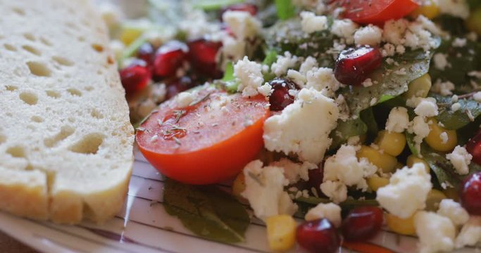 Fresh made corn salad with cherry tomatoes, soft cheese, sweetcorn kernel and pomegranate seed on plate on rotating stand, close up