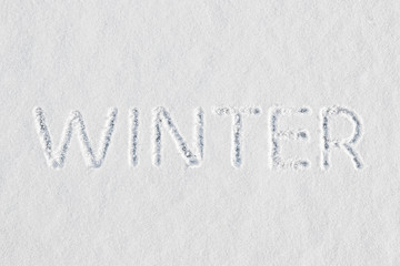 The word winter written in fresh snow at the threshold of the end of autumn and before the start of the New Year and Christmas holidays