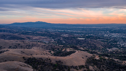 Fototapeta na wymiar Aerial view of open rolling hills in suburban Southern California. Radio tower atop hill during sunset surrounded by mountains and ocean