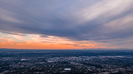 Aerial view of open rolling hills in suburban Southern California.  Radio tower atop hill during sunset surrounded by mountains and ocean