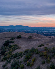 Aerial view of open rolling hills in suburban Southern California.  Radio tower atop hill during sunset surrounded by mountains and ocean