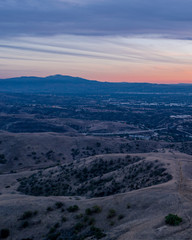 Aerial view of open rolling hills in suburban Southern California.  Radio tower atop hill during sunset surrounded by mountains and ocean