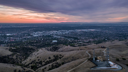 Aerial view of open rolling hills in suburban Southern California.  Radio tower atop hill during sunset surrounded by mountains and ocean