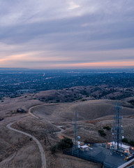 Aerial view of open rolling hills in suburban Southern California.  Radio tower atop hill during sunset surrounded by mountains and ocean