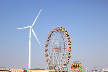 A huge ferries wheel and wind energy fan on a blue sky