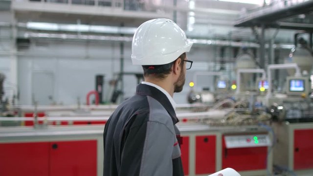 caucasian young bearded professional workman male engineer man people in hard hat with drawing working on engineering background on manufacture plant indoors. worker architect inspection, slow-mo 4 K