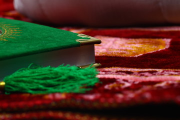 Green Al-Quran, Moslem Holy Book with arabic letters on a red praying rug