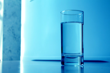 a glass of water stands on a table in blue