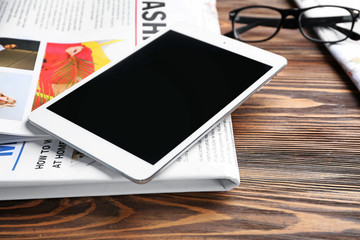 Newspaper and tablet computer on wooden background, closeup