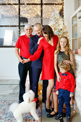 Portrait of beautiful big happy family in red clothes playing wih dog in a New Year's decorated studio. Happy christmas and new year concept