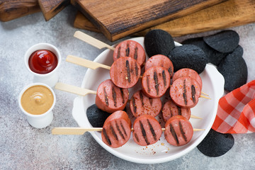 Brochettes of grilled chopped sausages with black potato chips over beige stone background