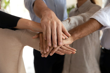 Close up international teammates joining hands together.