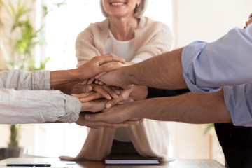 Close up happy diverse colleagues putting hands together.