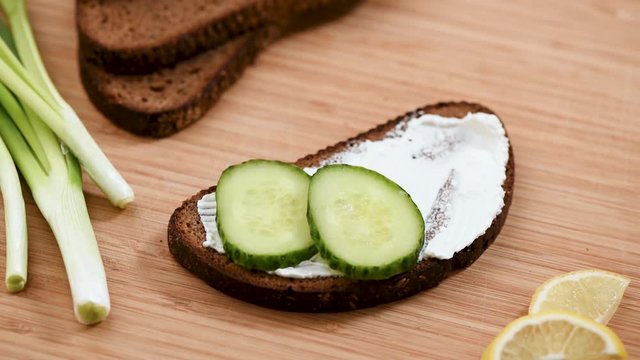 Closeup view of female chef preparing healthy sandwich with rye bread, cream cheese and cucumber. Female hand put cucumber on bread with cheese