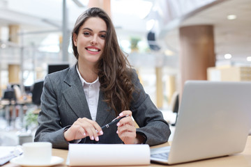 Portrait of a cheerful young businesswoman sitting at the table in office and looking at camera.