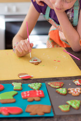 A girl decorates fresh baked homemade Chritstmas gingerbread cookie with icing. Selective focus