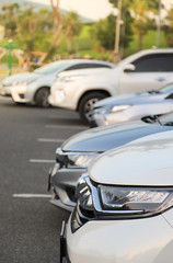 Closeup of front side of white car and other cars parking in out door parking lot with natural background in twilight evening.
