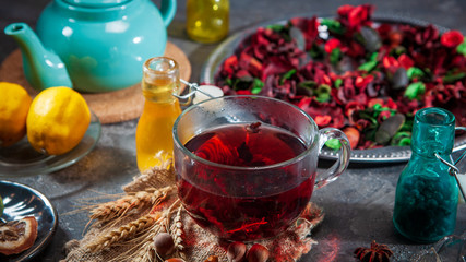 Red Hot Hibiscus tea in a glass mug on a wooden table among rose petals and dry tea custard with metallic heart