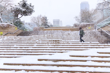 Woman is wearing winter coat and boots walking on the stairs covered with snow. Downtown vancouver covered with snow in winter time