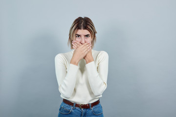 Young attractive blonde woman wearing white clothes, over isolated gray wall with surprise facial expression, covering mouth with hands