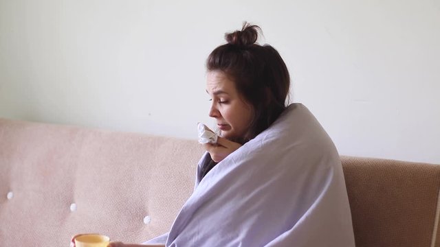 Sick young woman sitting at home with a runny nose and she sneezes