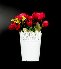 artificial red flowers in a paper pot on a black background