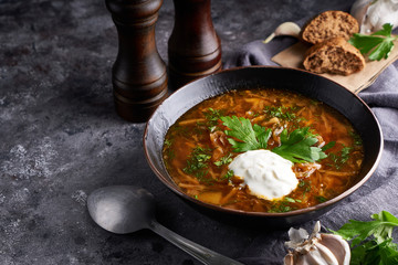 Traditional European and Russian soup borsch with cabbage, sour cream and meat served in a plate on a dark stone table