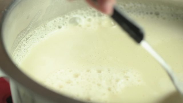 Preparation for making Tofu, skimming hot soy milk in pot with a ladle.
