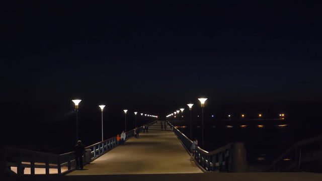 Unrecognizable people walking in the dark on Baltic sea bridge after sunset in Palanga tourist resort, Lithuania.