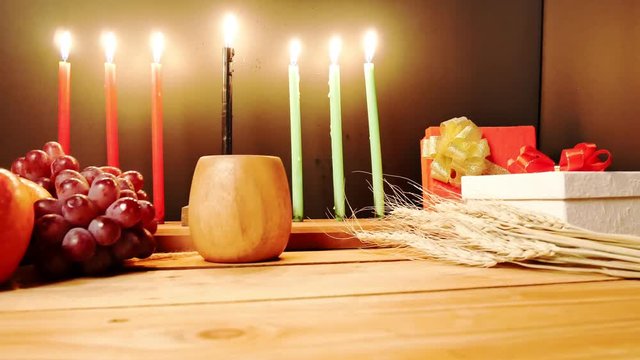 Kwanzaa celebration with decoration seven candles red, black and green, gift box, pumpkin, corn and fruit on wooden desk and background. 