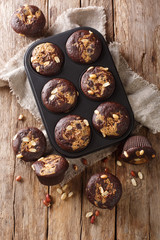 Obraz na płótnie Canvas Freshly baked chocolate muffins with peanut butter and nuts in a baking dish. Vertical top view
