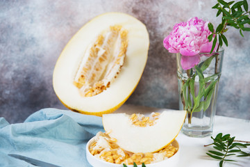 Still life of pieces of fresh juicy melon and pink flower on the table. Melon in a plate is on the table, decorated with flowers and leaves.