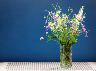 bouquet of wild flowers in a glass vase on a dark blue background.