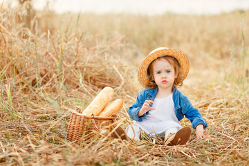 Naklejka na ściany i meble Portrait of a sweet beautiful little girl in straw hat sitting in a wheat field and makes a funny face. Happy childhood concept