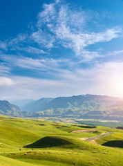 Fototapeta premium Peaceful landscape with meadow, hills, mountains and sunlight