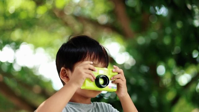 Asian child takes photo with toy camera on nature green bokeh background