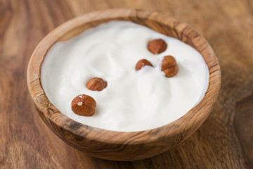 Fototapeta na wymiar Yogurt with hazelnuts in olive wood bowl on wooden table