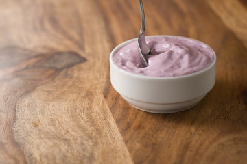 eating blueberry yogurt from white bowl on wood table