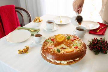 Woman put hot chocolate and Roscon de reyes, spanish Christmas cake  on table to celebrate Epiphany...